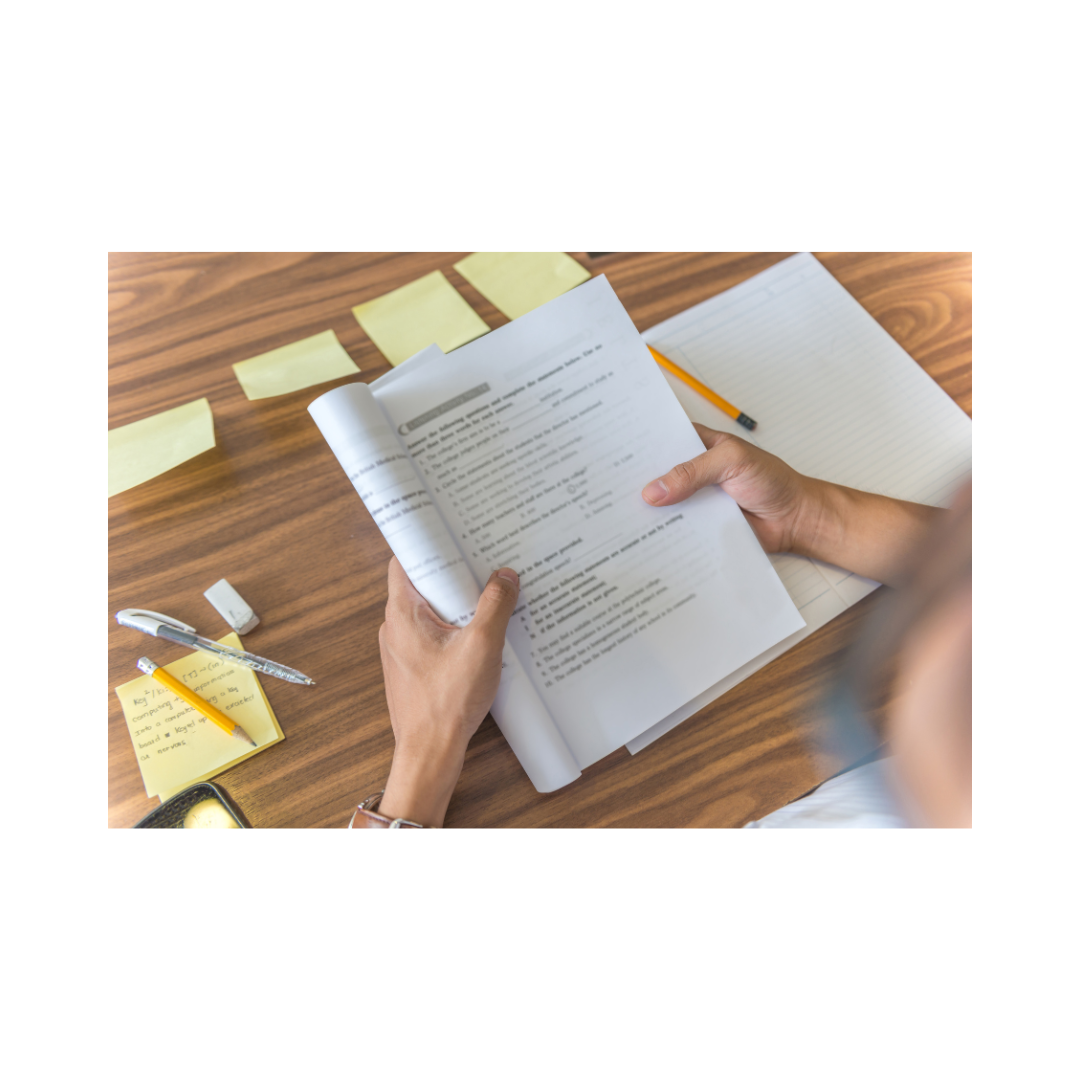 A toddler's hand holding an open workbook with unfinished exercises, surrounded by sticky notes and a pen on a table.