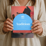 Person holding a book titled 'The Complete Audition Journal' with a red cover and blue front cover.