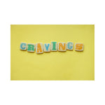 A colorful cookie decorated with letters spelling out the word 'CRAVINGS' on a yellow background.