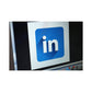 The image shows the LinkedIn logo, which is a blue square with a white arrow and the letter 'L' inside it, on a monitor or screen.