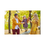 A family spending time outdoors, with a child being held by an adult, all dressed in fall clothing, surrounded by leaves on the ground.